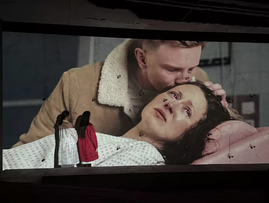dwie aktorki stoją przy ścianie, na której wyświetlany jest kadr z filmu z płaczącą kobietą, którą mężczyzna całuje w czoło