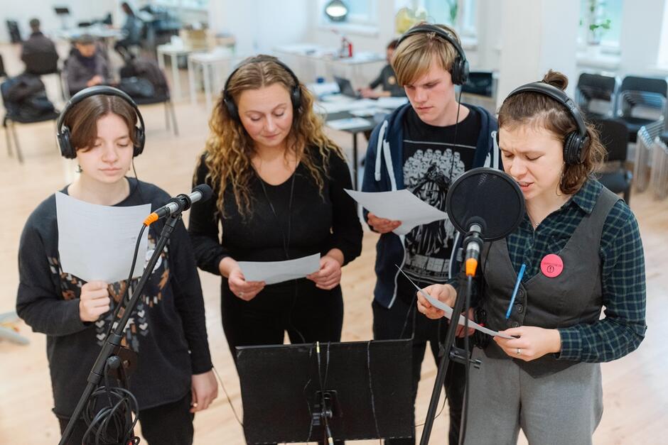 troje nastolatków i kobieta w starszym wieku w słuchawkach na uszach, śpiewają do mikrofonów