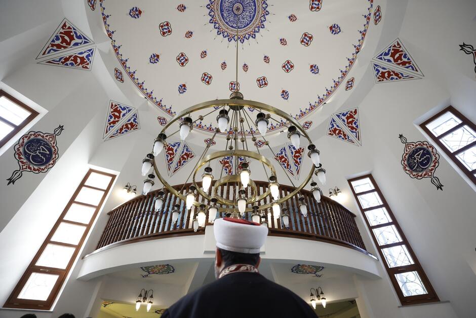 na zdjęciu tył głowy duchownego islamskiego z charakterystycznym białym turbanem, nad nim widać wiszący ogromny świecznik