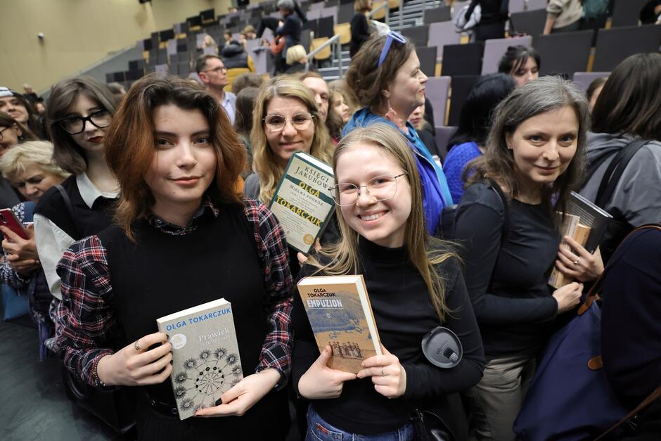 Młode i starsze kobiety stoją w kolejce trzymając różne książki Olgi Tokarczuk, np Bieguni i księgi Jakubowe