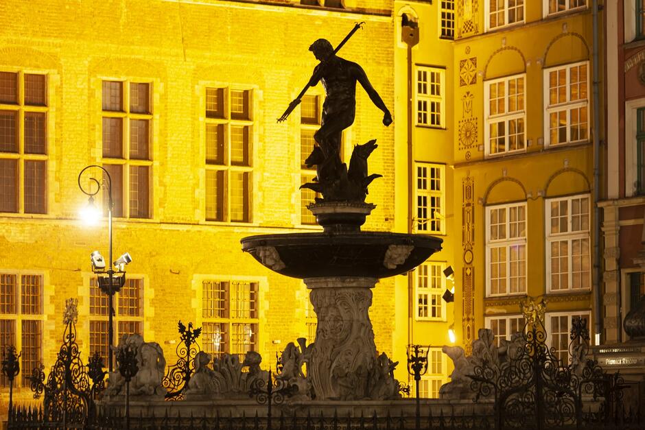 fontanna z posągiem mężczyzny w muszli, na tle rozświetlonego na żółto budynku