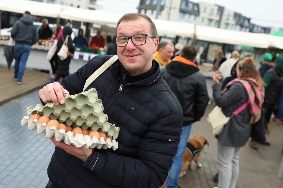 na zdjęciu mężczyzna w średnim wieku, trzyma jajka w specjalnym opakowaniu, uśmiecha się do fotografującego