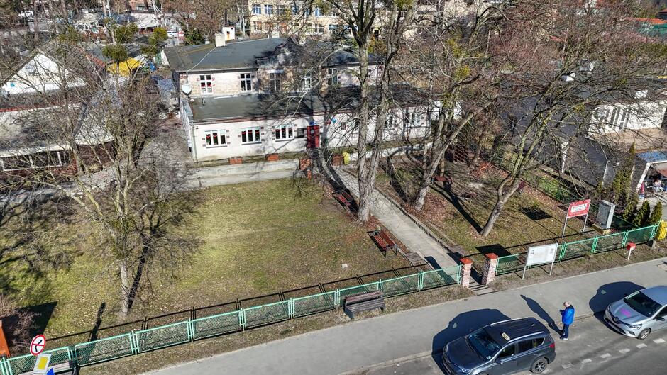 Zdjęcie zrobione dronem, z powietrza. Widać ziemny plac, w którego głębi znajdują się dwa budynki w starym stylu