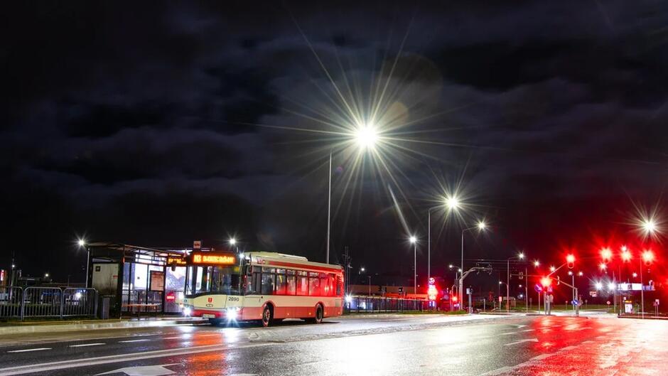 Noc, oświetlony przystanek autobusowy, na którym stoi autobus