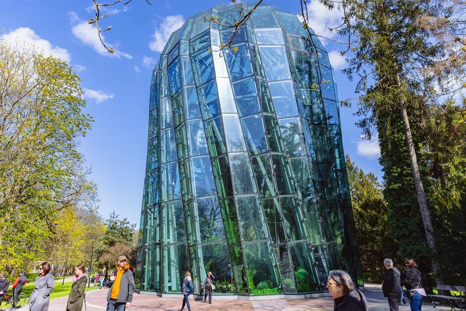 na zdjęciu szklana ogromna rotunda, to palmiarnia parkowa, widać też spacerujących ludzi