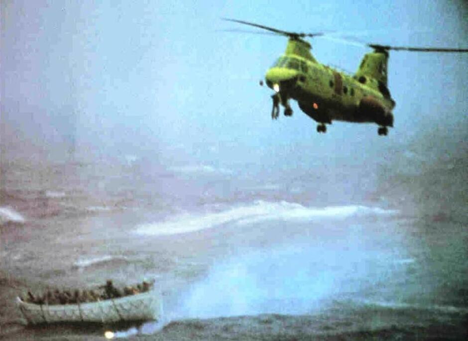 Wojskowy helikopter nad morzem, wśród fal łódź ratunkowa z ludźmi na pokładzie