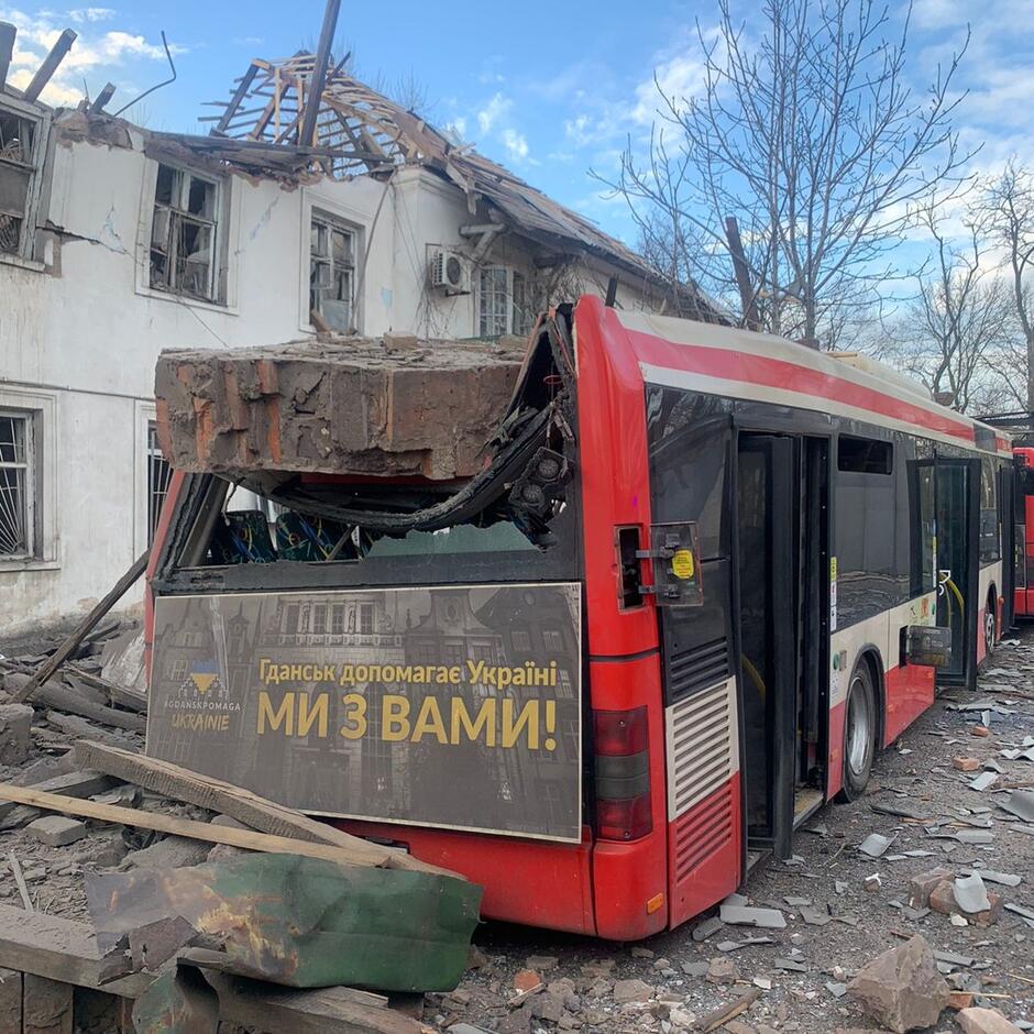Zniszczony i spalony autobus obok budynku rozbitego przez ostrzał rakietowy