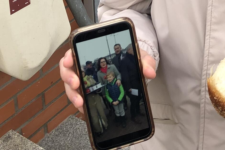 Ekran telefonu komórkowego, na nim widać zdjęcie. Mały chłopiec stoi przed prezydent Dulkiewicz, po prawej stoi wysoki mężczyzna - wiceprezydent Piotr Grzelak