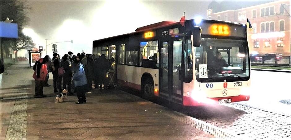 Czerwono-biały autobus miejski marki Mercedes z numerem bocznym 2753 i rejestracją GD 689RJ. Wyświetlacz nad przednią szybą ponownie pokazuje napis "S.O.S.". Autobus zatrzymał się przy przystanku. Widać grupę osób, które czekają na wejście do autobusu, w tym jedną osobę z psem. Jest mgła, światła autobusu przebijają się przez mgłę, tworząc efekt halo. 