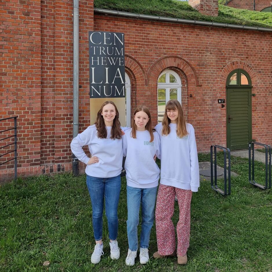 Trzy dziewczęta w wieku licealnym stoją jedna obok drugiej, pozując do zdjęcia