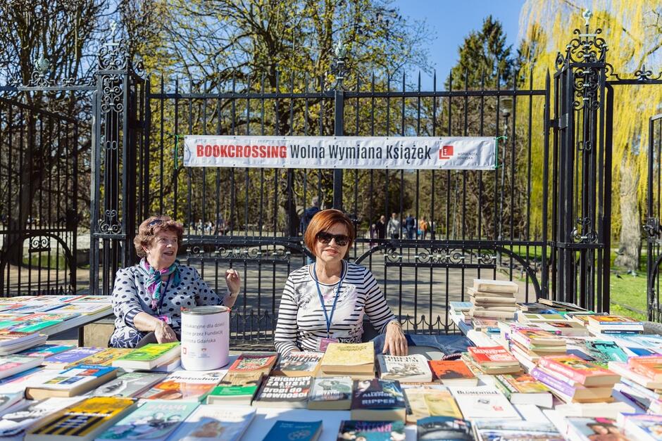 dwie kobiety za stołami wyłożonymi książkami, za nimi napis bookcrossing wolna wymiana książek