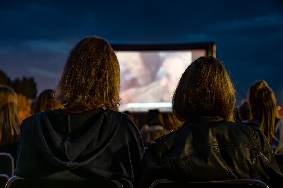 zdjęcie robione chłopakowi i dziewczynie, którzy oglądają film, od tyłu - za nimi projektor z wyświetlanym filmem