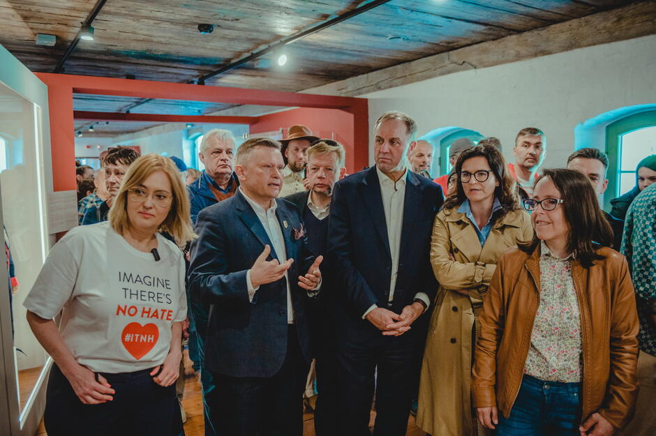 Grupa samorządowców i polityków zwiedza wystawę w odrestaurowanych Koszarach Napoleońskich. Oprowadza ich dyrektor Muzeum Gdańska.