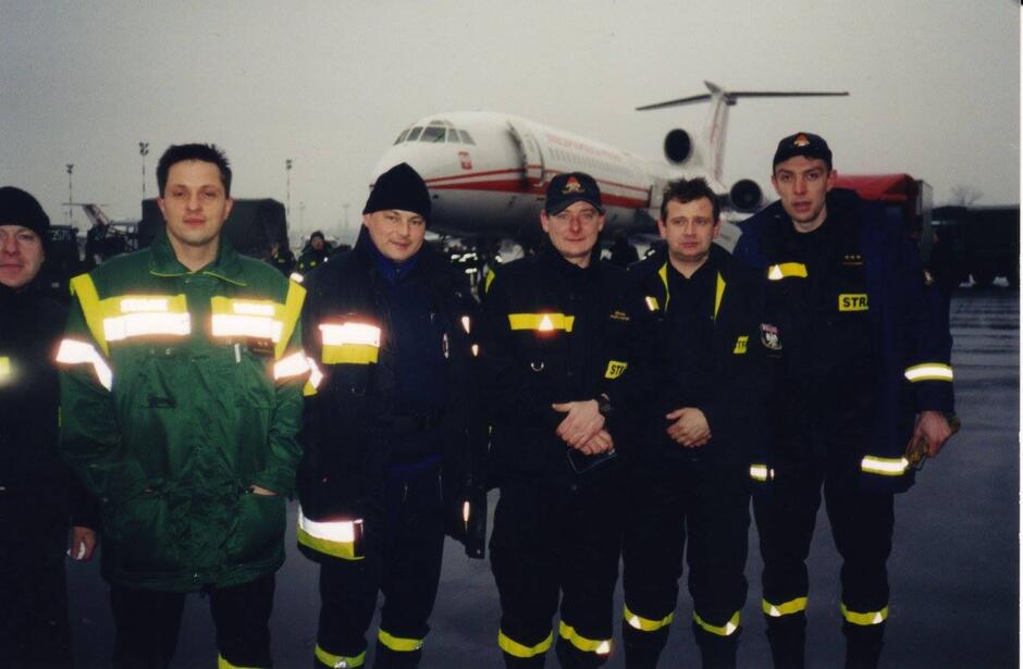 Sześciu strażaków w mundurach pozuje do zdjęcia na tle samolotu.