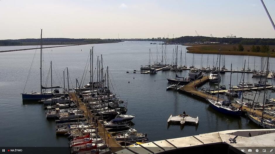 Zrzut ekranu z kamery miejskiej. Widok na przystań jachtową na rozlewisku rzeki. W marinie zacumowane jachty.