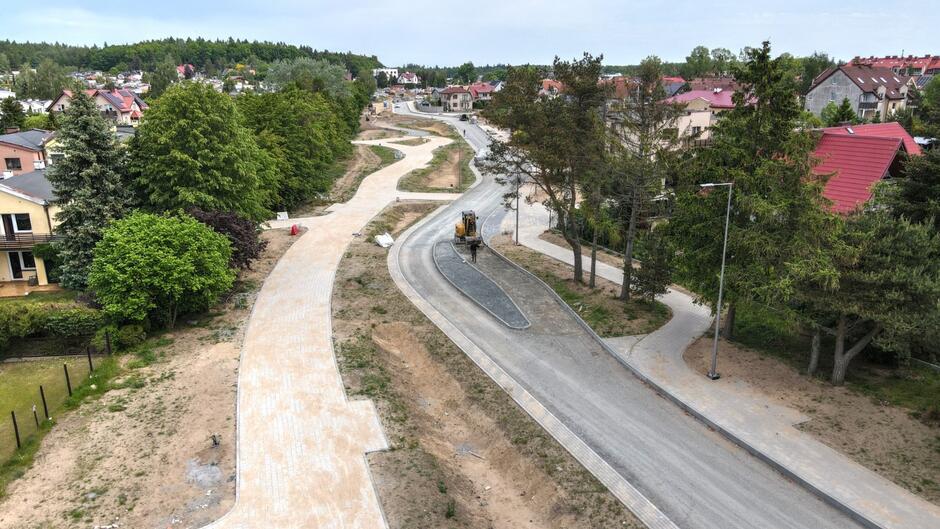 zdjęcie z drona, widać plac budowy na którym powstaje nowa ulica, w tle zabudowa jednorodzinna