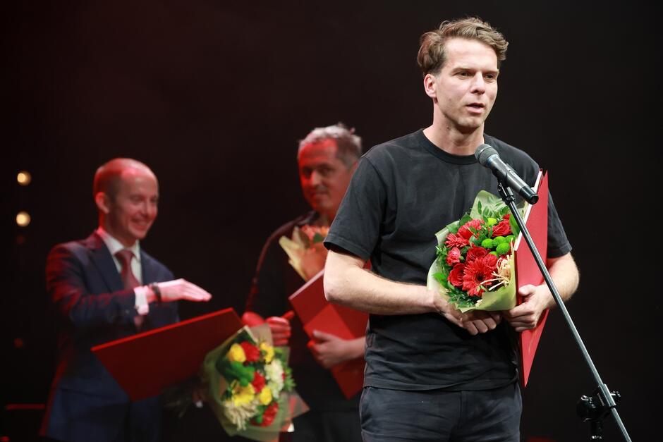 mężczyzna po 30-tce, trzyma bukiet kwiatów, mówi do mikrofonu