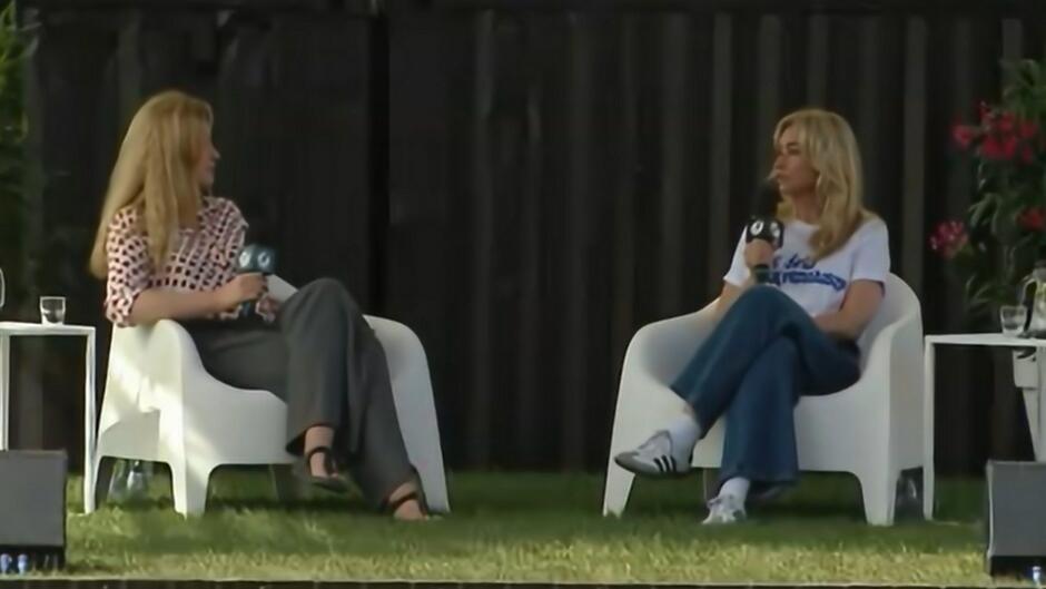 na zdjęciu scena, na niej siedzą dwie kobiety w średnim wieku, na białych fotelach, rozmawiają ze sobą