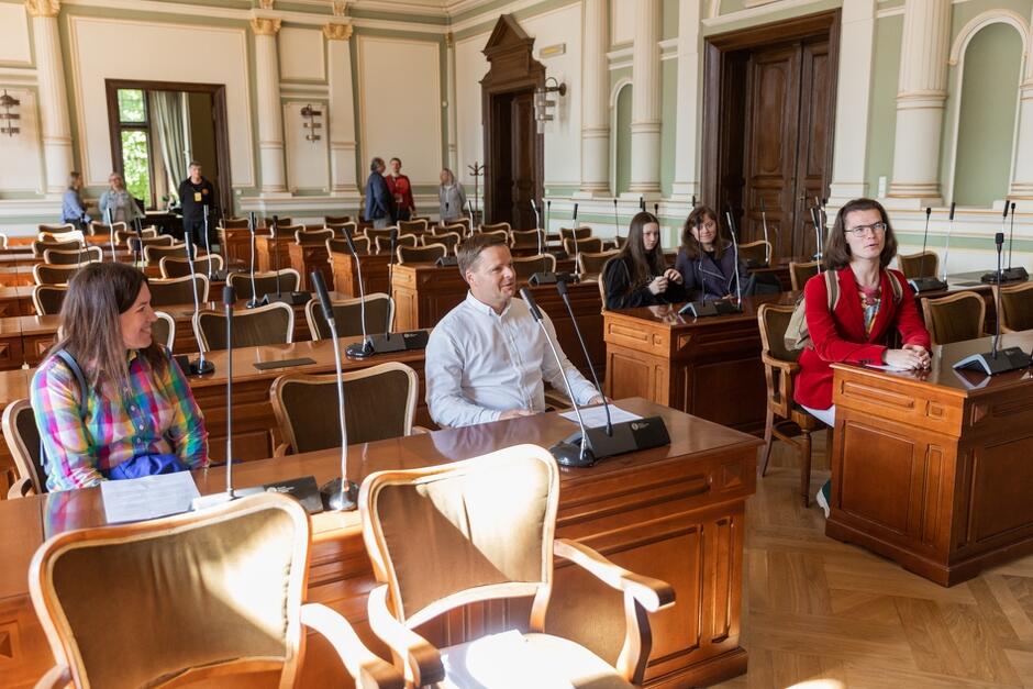 Na zdjęciu ludzie siedzą za stołami w siedzibie rady miasta 