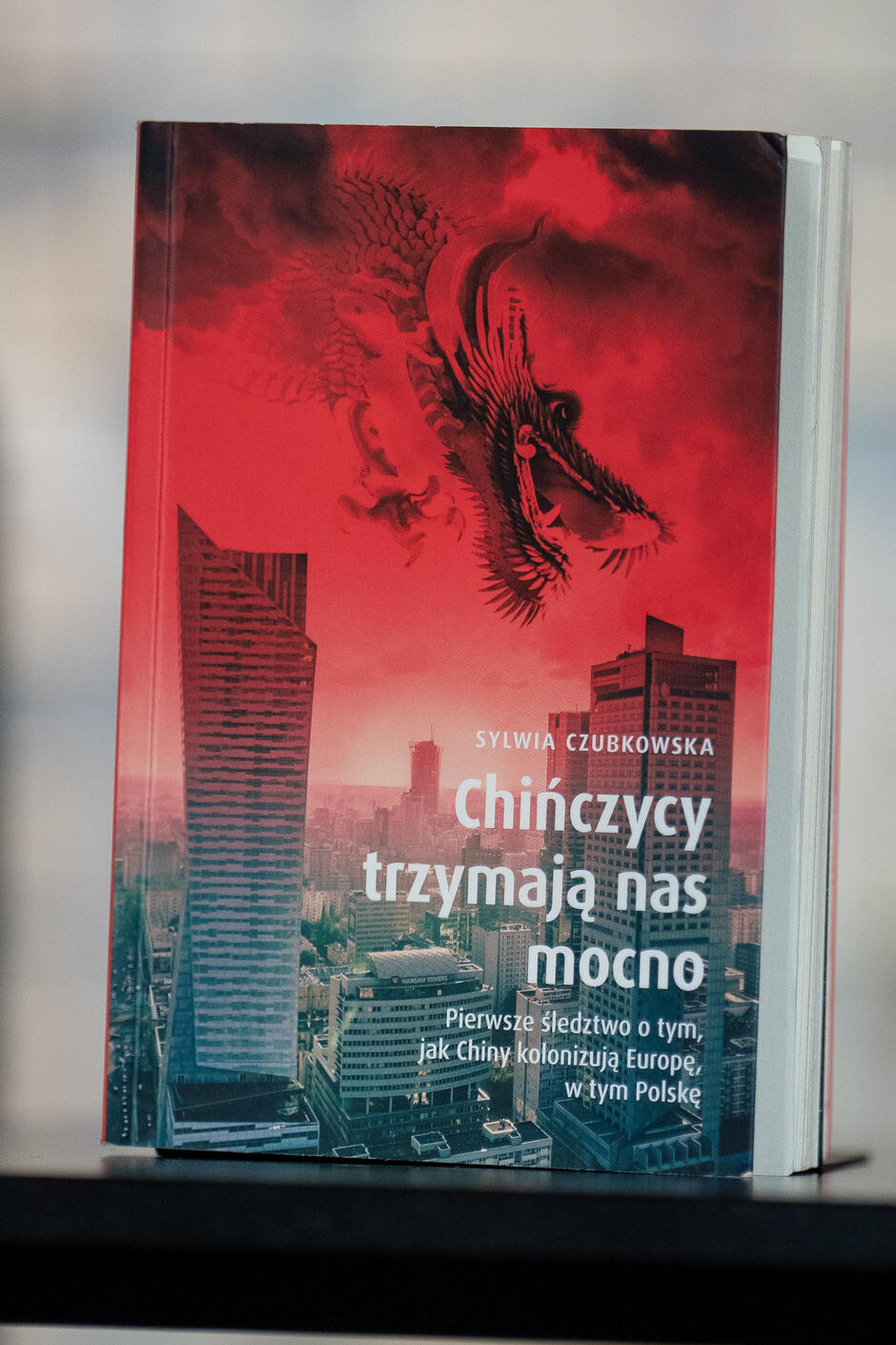 Okładka książki Sylwii Czubkowskiej „Chińczycy trzymają nas mocno. Pierwsze śledztwo o tym, jak Chiny kolonizują Europę, w tym Polskę”. Na okładce widać wieżowce, nad którymi leci chiński smok.