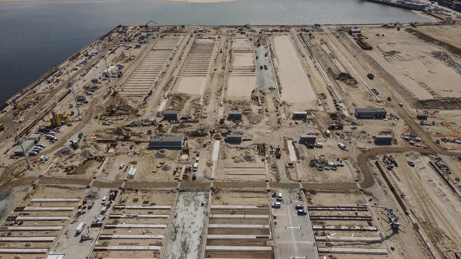 Na zdjęciu widać z lotu ptaka szczegółowy widok prac budowlanych nad nowym nabrzeżem T3 w terminalu kontenerowym Baltic Hub. Liczne maszyny, kontenery i rozległe wykopy pokazują zaawansowany etap budowy, zorganizowany na dużym obszarze przy wodzie.