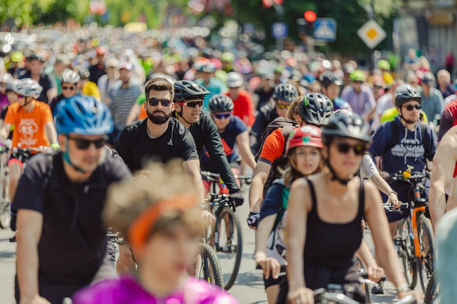 Na zdjęciu widać dużą grupę rowerzystów jadących w zorganizowanym przejeździe ulicznym. Większość uczestników nosi kaski, a atmosfera wygląda na radosną i pełną energii, z ludźmi różnych wieków i stylów jazdy.
