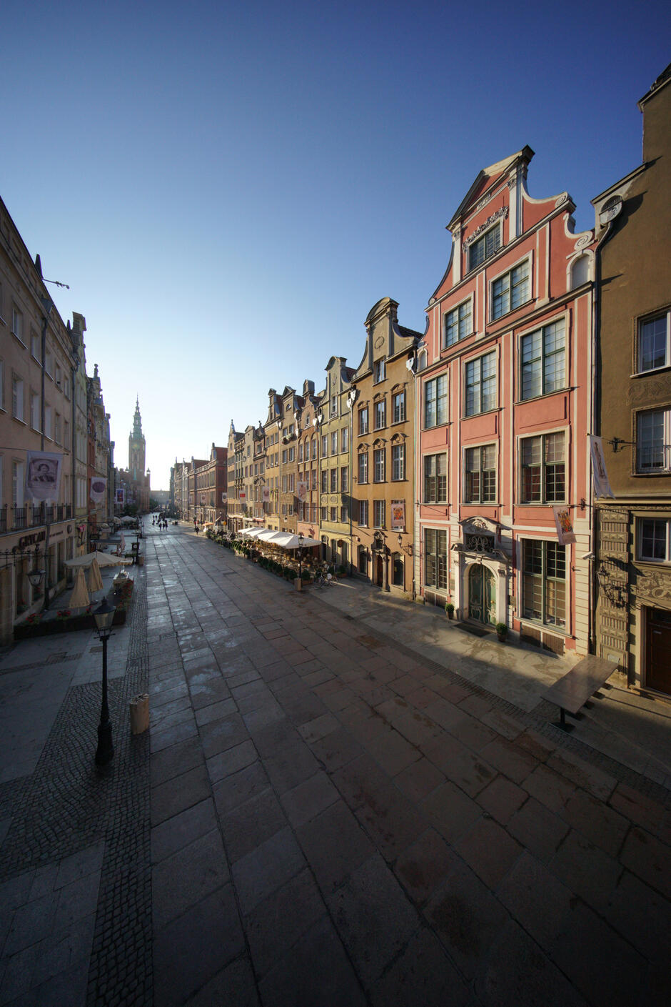 Zdjęcie przedstawia ulicę Długą w Gdańsku, widzianą od strony wejścia do Domu Uphagena, sfotografowaną przez Dariusza Kulę. Po obu stronach ulicy znajdują się kolorowe kamienice, a w tle widać wieżę Ratusza Głównego Miasta