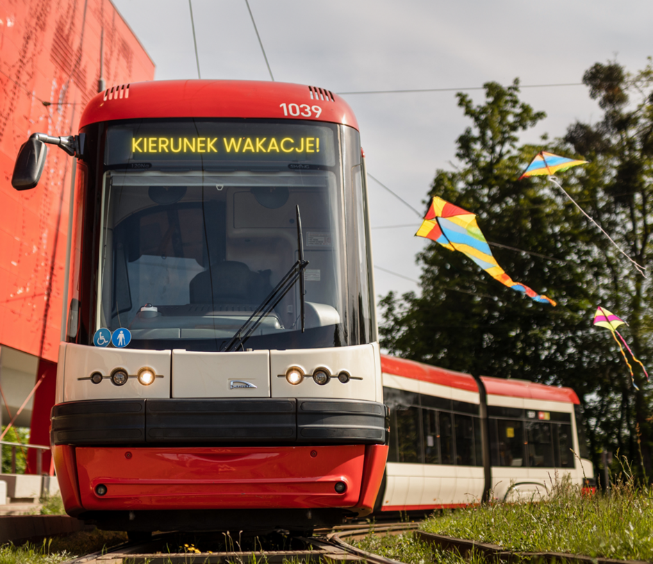 na zdjęciu tramwaj na torach, w kolorach czerwonym, kremowym i czarnym, na przedniej szybie wyświetla się napis kierunek wakacje