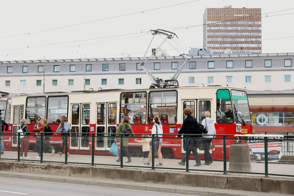 Na zdjęciu widać centrum miasta, przystanek tramwajowy, ludzie stoją na przystanku, na dalszym planie zabudowania 