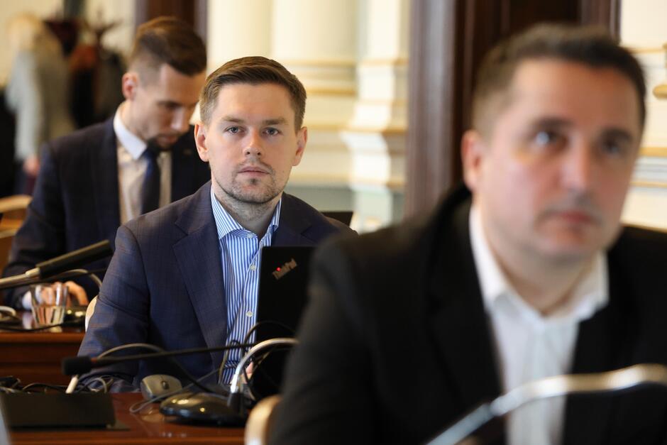Zdjęcie młodego mężczyzny, który siedzi za stołem podczas obrad Rady Miasta Gdańska ubiegłej kadencji 