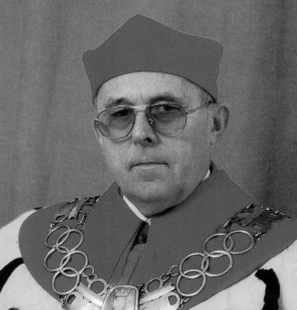 Czarno-białe zdjęcie: twarz mężczyzny w okularach, na szyi łańcuch rektorski, na głowie czapka rektora
