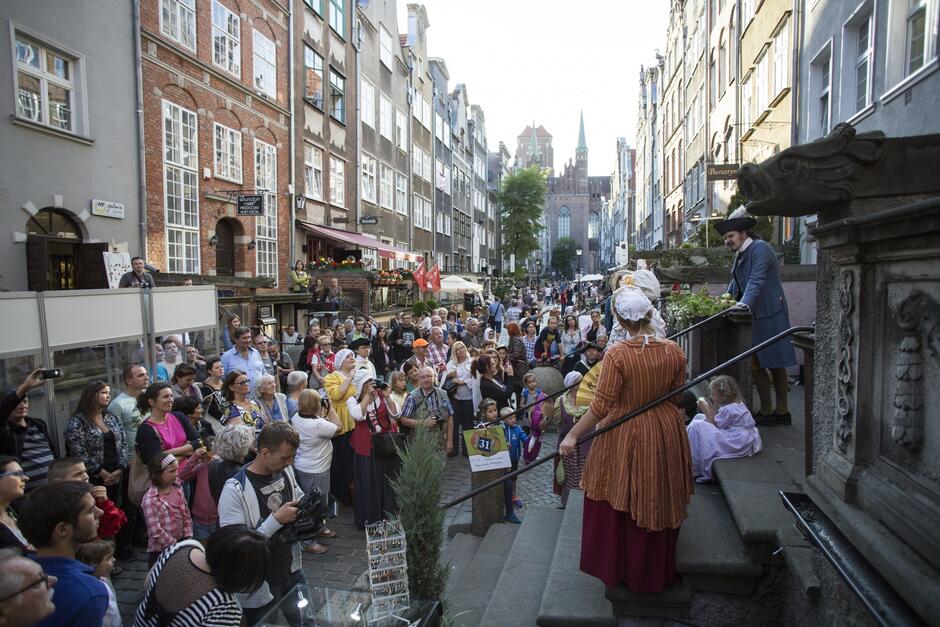 Tłum ludzi na renesansowej ulicy Mariackiej w Gdańsku. Ludzie oglądają przedstawienie osób ubranych w stroje z epoki.