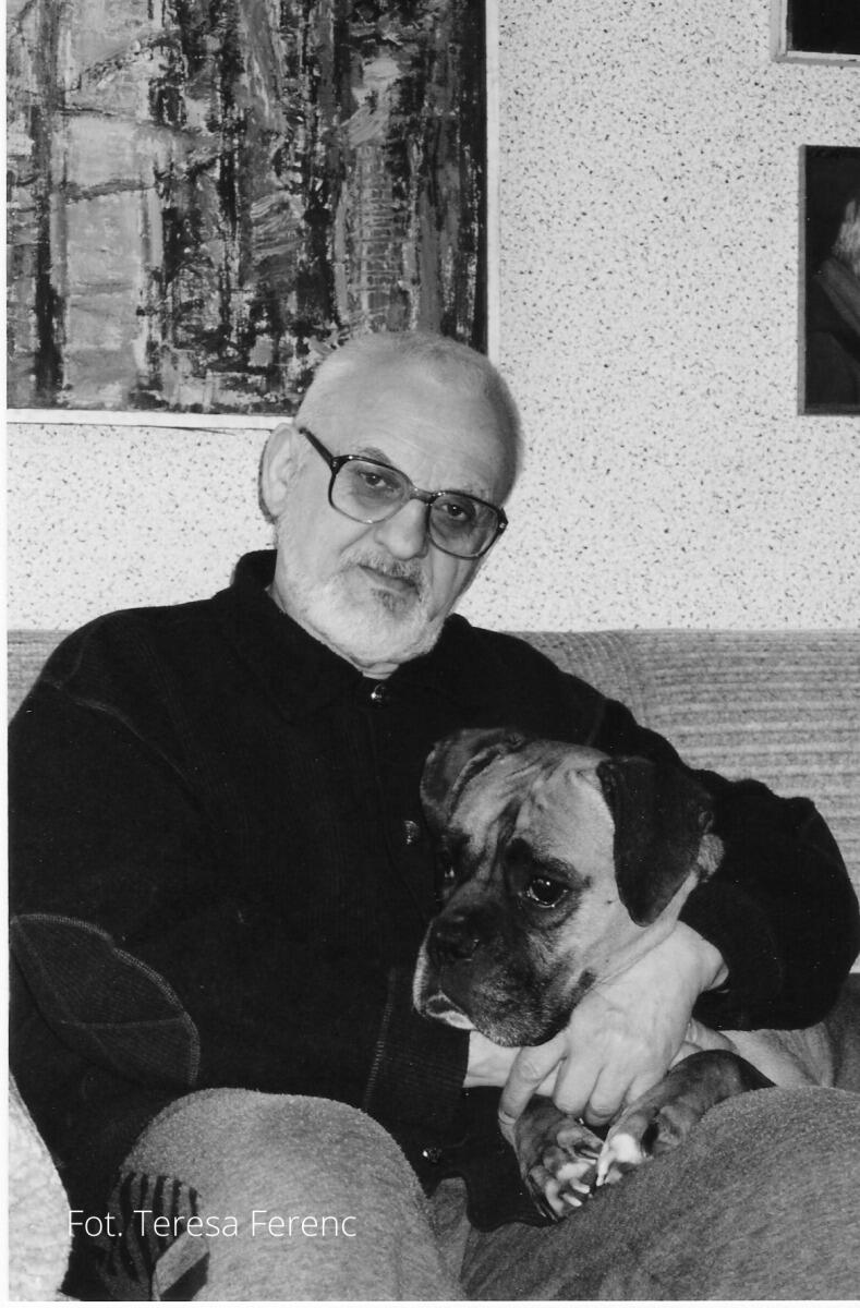 Na zdjęciu widzimy starszego mężczyznę z białą brodą i w okularach, siedzącego na kanapie i trzymającego na kolanach psa rasy bokser. W tle znajduje się abstrakcyjny obraz, a zdjęcie zostało wykonane przez Teresę Ferenc, co jest zaznaczone w lewym dolnym rogu fotografii
