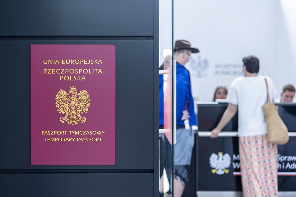 Widok plakatu przedstawiającego okładkę paszportu - po lewej. Po prawej są trzy osoby załatwiające formalności paszportowe 