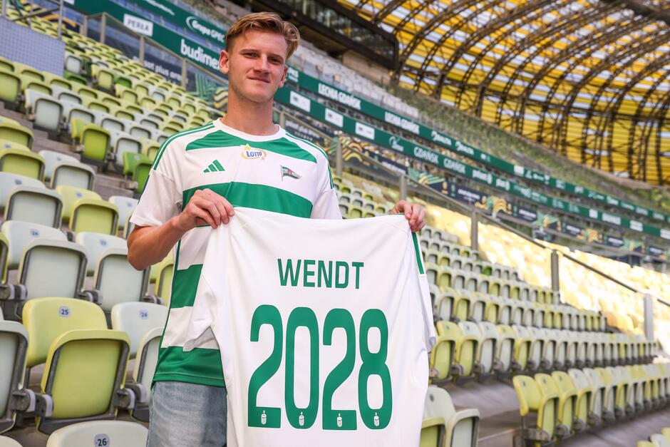 Młody piłkarz trzyma w rękach biało-zieloną koszulkę z liczbą 2028