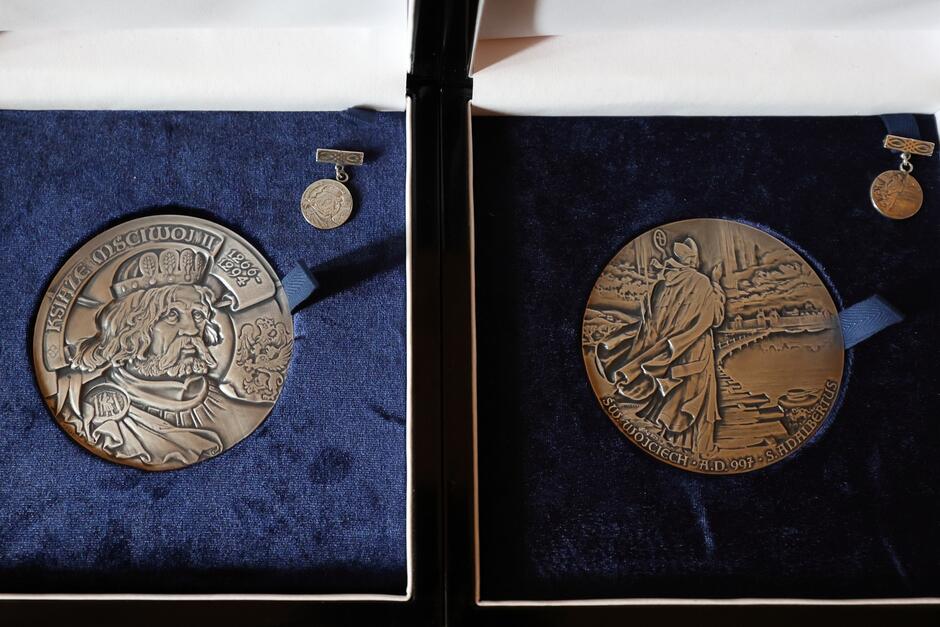 Dwa medale w kształcie kół wykonane z metalu leżą obok siebie na aksamitnej wyściółce.
