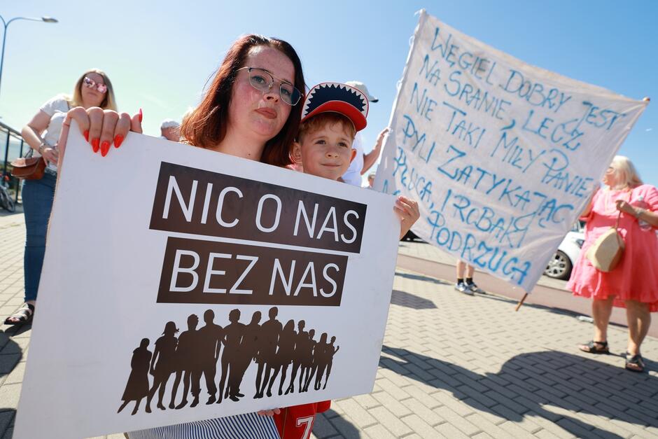 Kobieta z dzieckiem na rękach idzie w proteście i trzyma transparent z napisem Nic o nas bez nas .