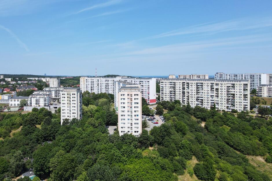 na zdjęciu osiedle wysokich bloków mieszkalnych, widać wysokie i szerokie bloki o jasnej elewacji