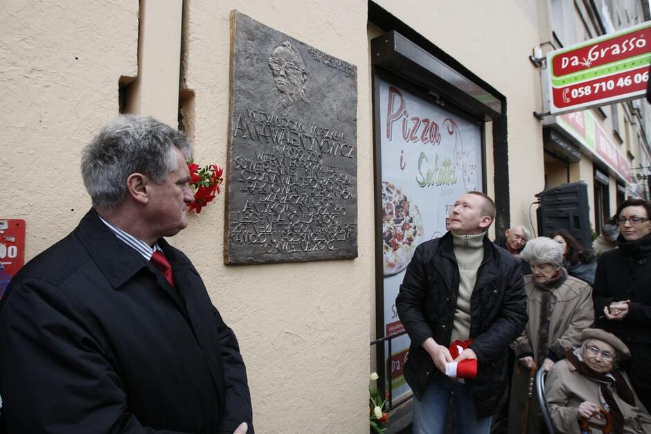 ludzie przy tablicy wiszącej na ścianie budynku