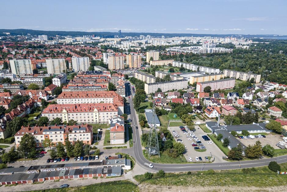 zdjęcie z drona, widać jedną z dzielnic, na pierwszym planie kamienice wielorodzinne, widać też garaże a także place parkingowe z samochodami, w tle wyższe budynki w tym bloki mieszkalne