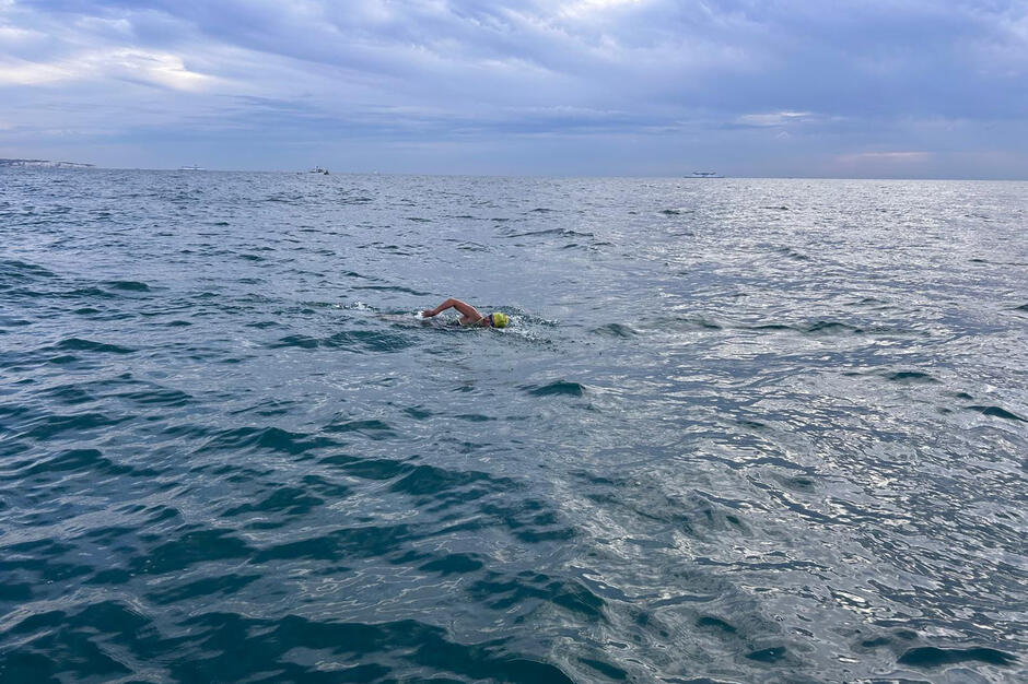 Kobieta w czepku na głowie płynie w morzu.