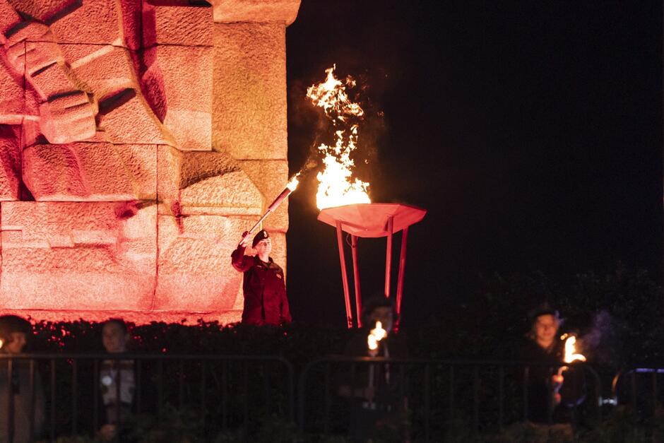 Harcerka z pochodnią stoi przy podstawie pomnika Westerplatte