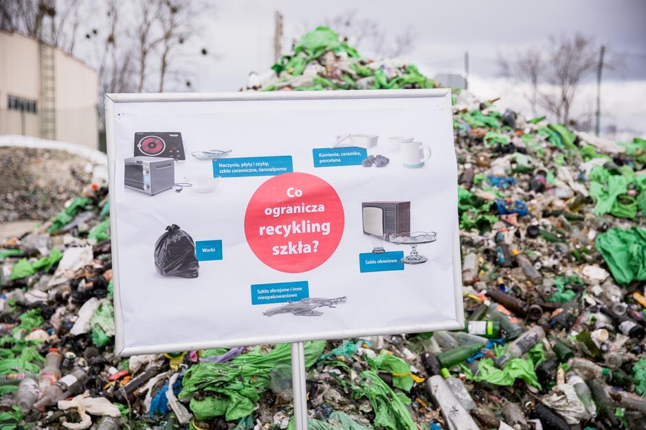 Stos śmieci. Przed nim plansza z napisem: Co ogranicza recykling szkła?