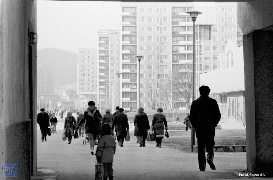 Archiwalne zdjęcie czarnobiałe z 1984 roku. Promenadą przez osiedle mieszkaniowe idą ludzie. Wokół bloki mieszkalne.