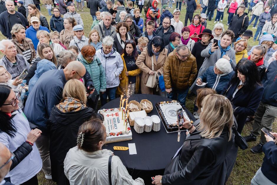 na zdjęciu widać grupę ponad trzydziestu osób, stoją wokół stołu, na którym stoją duże prostokątne dwa torty