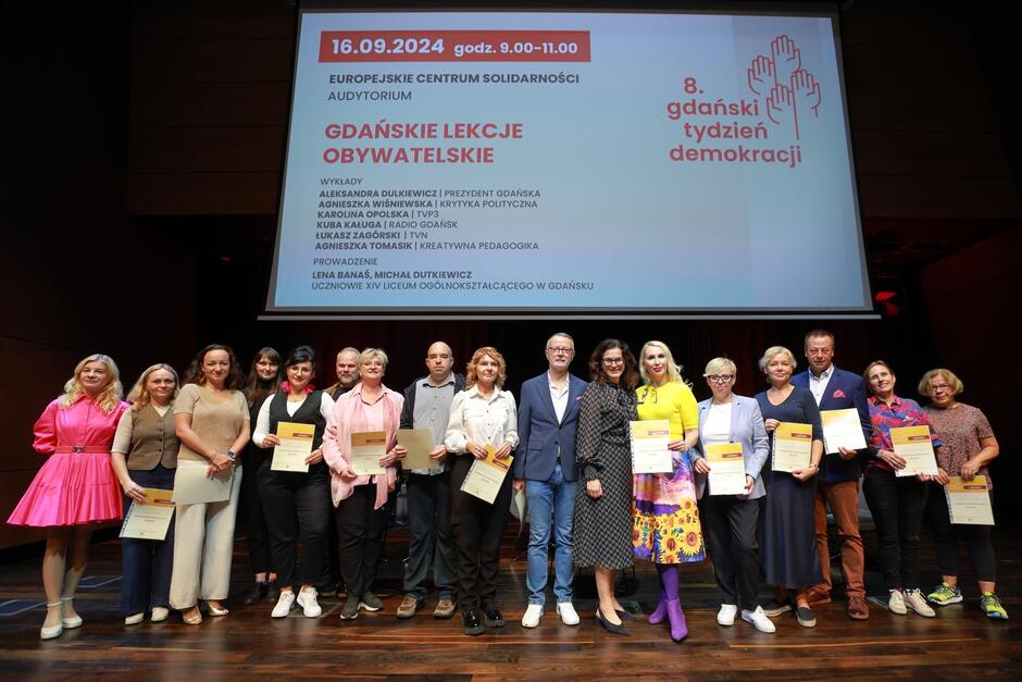 Kilkanaście osób stoi na scenie. Nad nimi telebim z programem Gdańskiego Tygodnia Demokracji