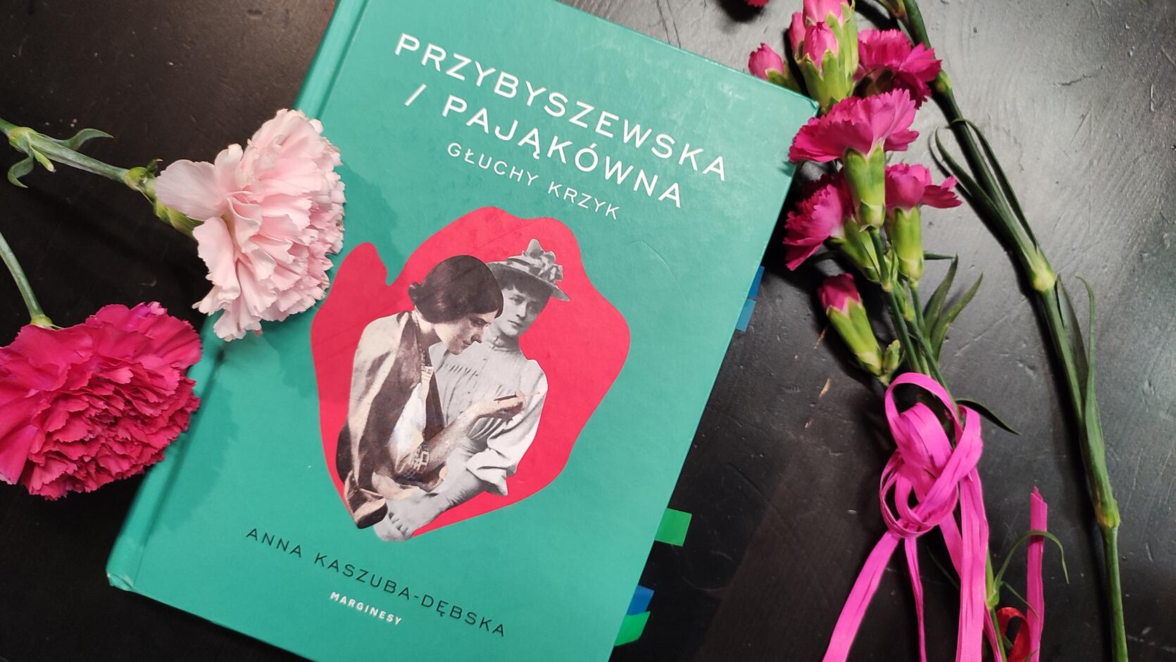 Okładka książki pt. "Przybyszewska / Pająkówna. Głuchy krzyk" jest zielona, w centralnym punkcie okładki różowy owal, a w nim portrety dwóch kobiet w strojach z początku XX wieku. Obok książki na stoliku leżą goździki