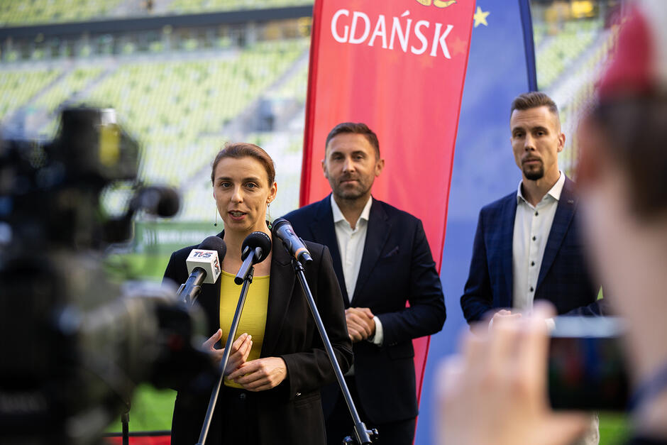 Kobieta mówi do mikrofonu na konferencji prasowej na stadionie.