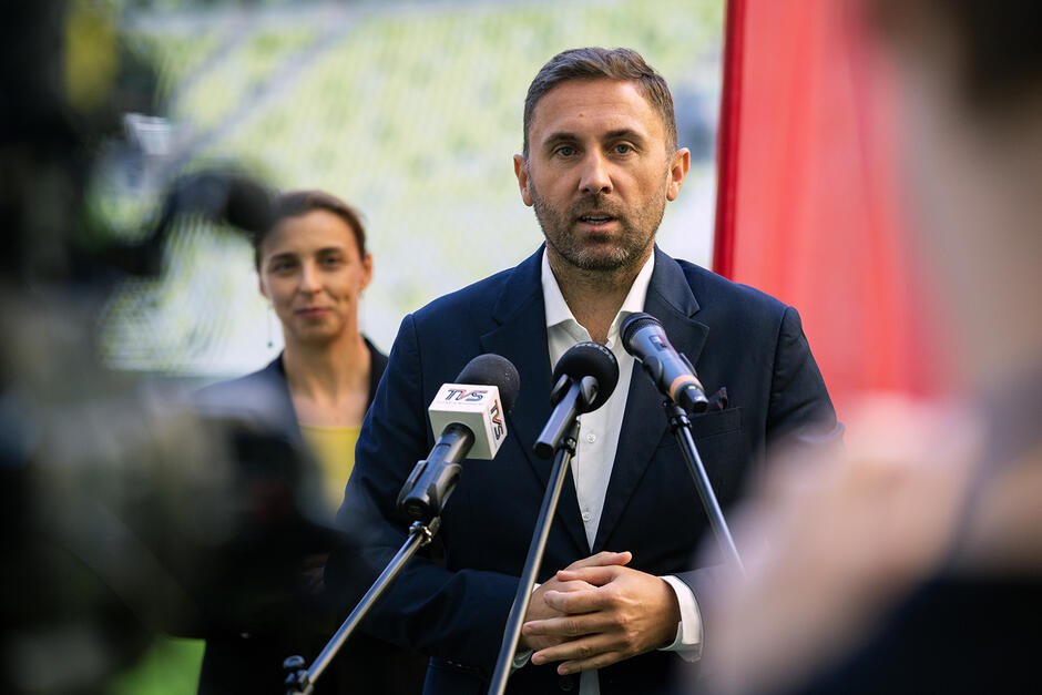 Mężczyzna mówi do mikrofonu podczas konferencji prasowej na stadionie.