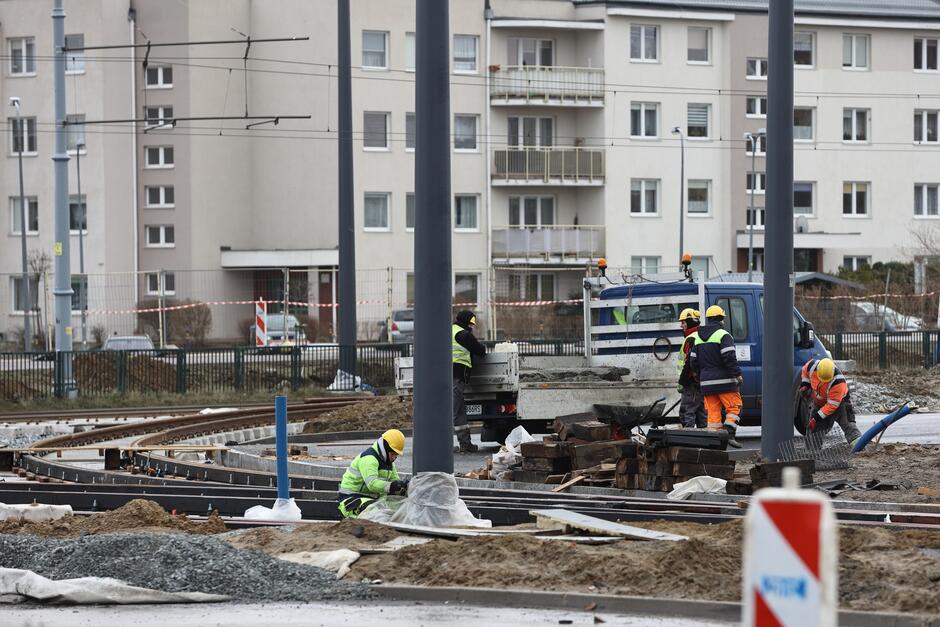 Robotnicy pracują przy budowie torów tramwajowych. W tle bloki mieszkalne.